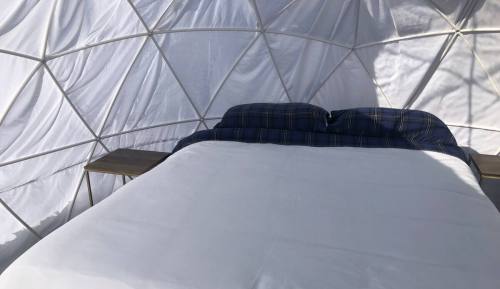 Interior of a geodesic dome featuring a neatly made bed with blue plaid pillows and wooden side tables.