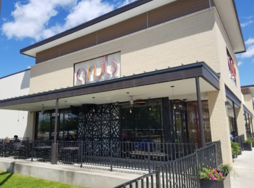 Exterior of a modern restaurant named "grub," featuring a patio and large windows under a blue sky.