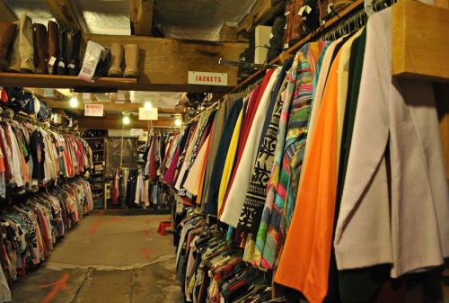 A cozy thrift store aisle filled with colorful clothing racks and shelves, showcasing jackets and various garments.