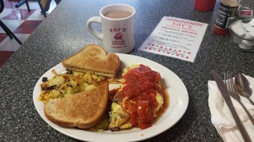 A plate of breakfast with an omelet topped with salsa, hash browns, toast, and a cup of coffee on a table.