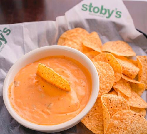A bowl of creamy cheese dip with a tortilla chip, served alongside a plate of crispy tortilla chips.