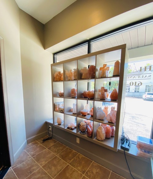 A display shelf filled with various salt lamps and crystal sculptures in a well-lit room.