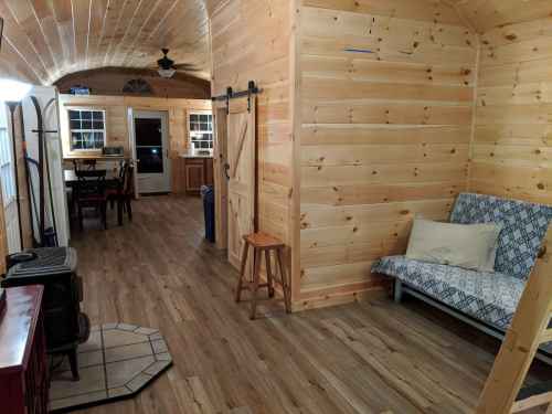 Cozy interior of a wooden cabin featuring a futon, dining area, and kitchen, with warm lighting and wooden walls.