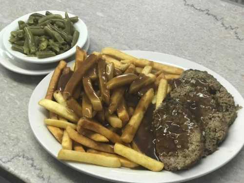 A plate of meatloaf with gravy, served with French fries and a side of green beans.