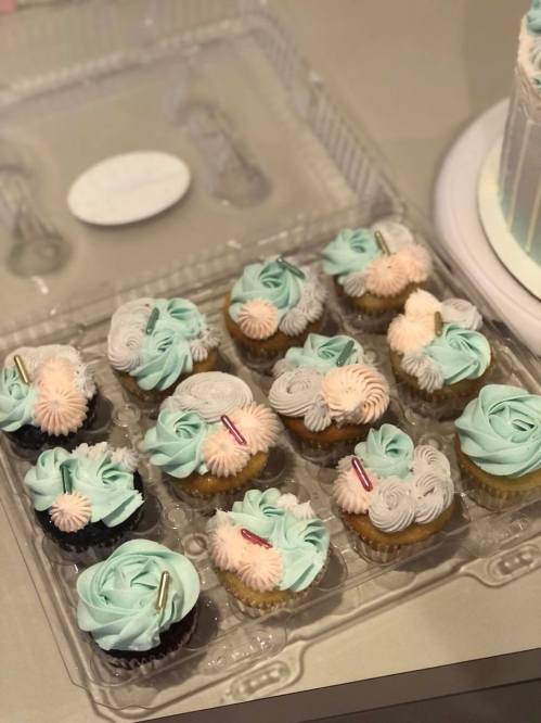 A tray of colorful cupcakes with mint green and pink frosting, decorated with swirls and sprinkles.