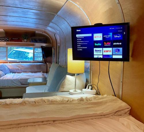 Cozy interior of a camper with a TV displaying streaming options, a lamp, and a bed in the foreground.