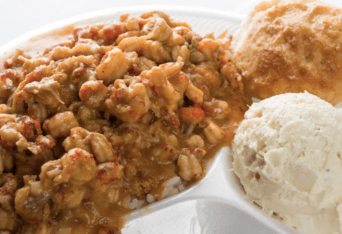 A plate of crawfish étouffée served over rice, accompanied by a biscuit and a scoop of creamy mashed potatoes.