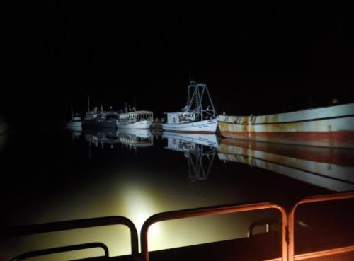 Boats docked at night, reflecting in calm water under dim lighting.