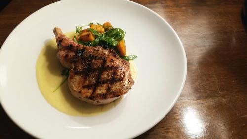Grilled pork chop on a plate with creamy sauce, sautéed greens, and roasted sweet potatoes.