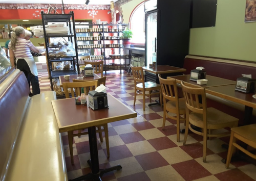 A cozy café interior with checkered floors, wooden tables, and a display shelf filled with products.