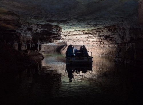 A group of people on a small boat in a dimly lit cave, surrounded by rock formations and calm water.