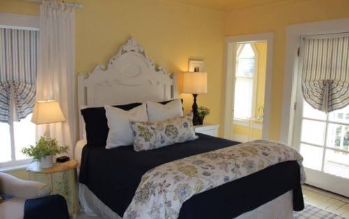 Cozy bedroom with a yellow wall, a large bed with floral bedding, a lamp, and a door leading to an outdoor area.