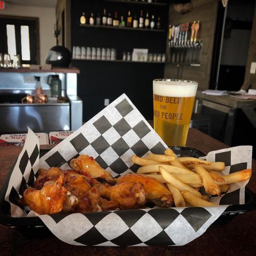 A basket of buffalo wings and fries next to a pint of beer in a cozy bar setting.