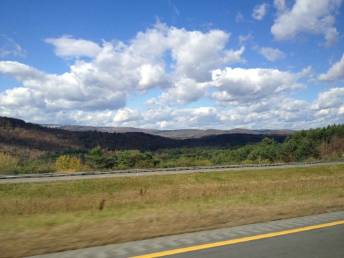 A scenic view of rolling hills and trees under a blue sky with fluffy white clouds.