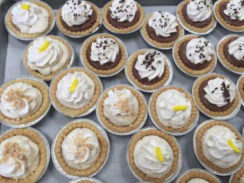 A tray of mini pies topped with whipped cream, chocolate shavings, and lemon slices, arranged in neat rows.