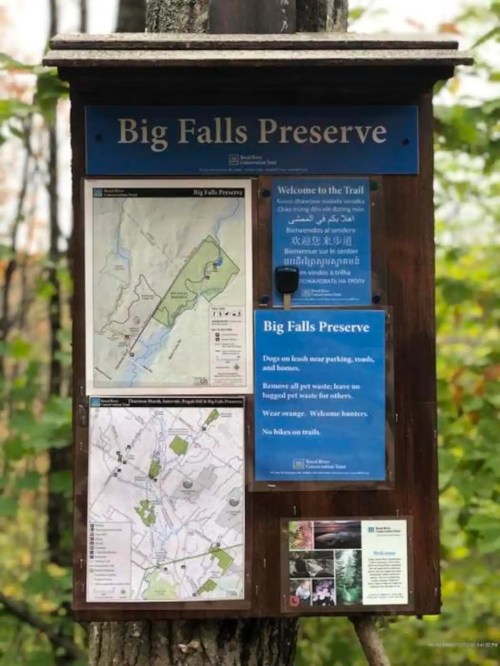 Trail sign for Big Falls Preserve, featuring maps and guidelines for visitors, surrounded by trees.
