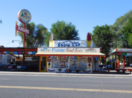 Colorful retro diner with "Snow Cap" sign, serving burgers, shakes, and root beer, located on Route 66.