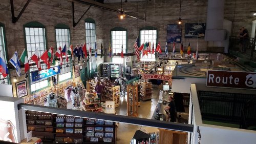 A spacious gift shop filled with international flags, souvenirs, and displays, featuring a Route 66 sign.