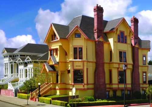 A colorful Victorian-style house with multiple chimneys, surrounded by greenery and a clear blue sky.