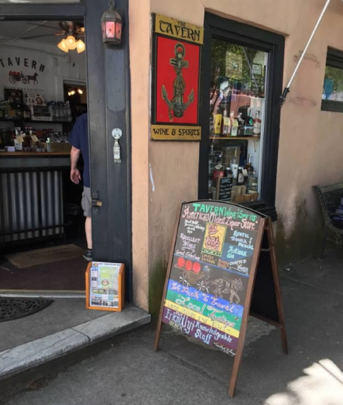 A storefront with a sign reading "Cavern Wine & Spirits" and a chalkboard menu outside. A person is entering the shop.