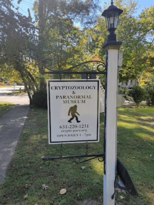 Sign for a Cryptozoology & Paranormal Museum, featuring a silhouette and contact information. Open daily 1-7 PM.