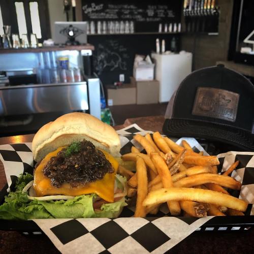 A cheeseburger with lettuce and a savory topping, served with a side of golden fries on a checkered plate.