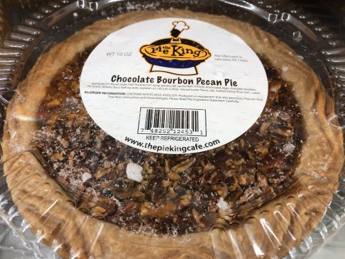 A chocolate bourbon pecan pie in a clear plastic container with a label from The Pie King.