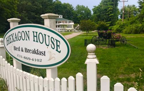 Sign for Hexagon House Bed & Breakfast with a green lawn and a vintage carriage in the background.