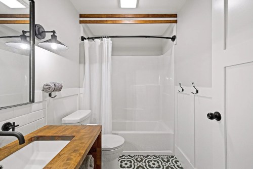 A modern bathroom featuring a shower, white walls, a wooden vanity, and patterned floor tiles.