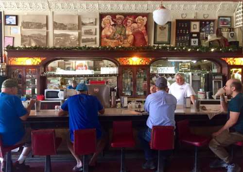 A vintage diner scene with patrons sitting at the counter, chatting and enjoying drinks, surrounded by nostalgic decor.