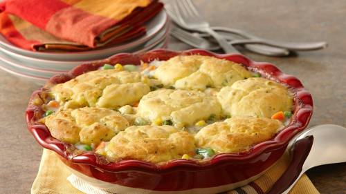 A red dish filled with chicken and vegetable stew topped with golden, fluffy biscuits, set on a table with colorful napkins.