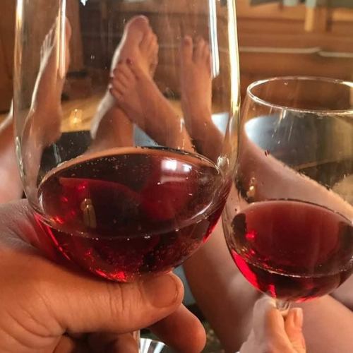 Two pairs of feet and glasses of red wine are visible, suggesting a relaxed, cozy atmosphere.