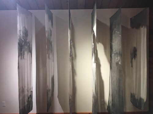 Abstract art installation featuring vertical fabric panels with gray and white designs, creating a layered effect.