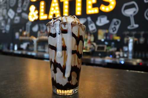 A tall glass of chocolate-drizzled ice cream topped with whipped cream, set against a bar backdrop.