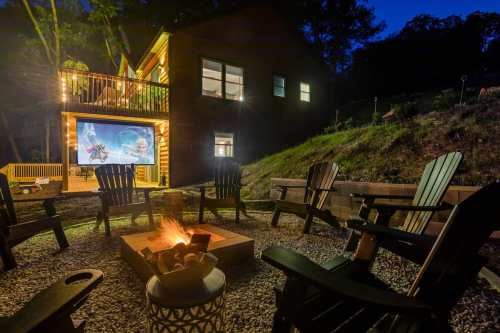 A cozy outdoor fire pit surrounded by chairs, with a house and a movie screen illuminated at night.