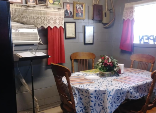 A cozy dining area with a table set for meals, surrounded by framed photos and curtains, featuring an air conditioner.