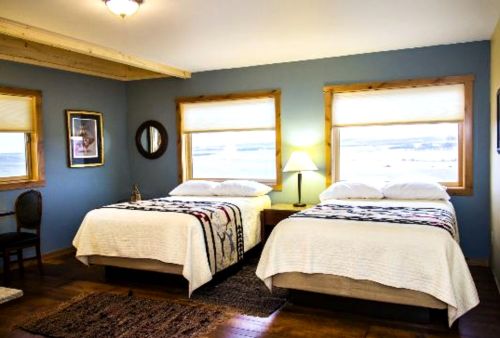 Cozy bedroom with two beds, wooden accents, and large windows letting in natural light.