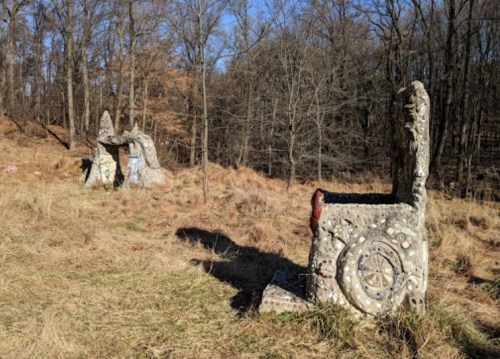 Two abstract stone structures in a grassy area surrounded by trees, under a clear blue sky.
