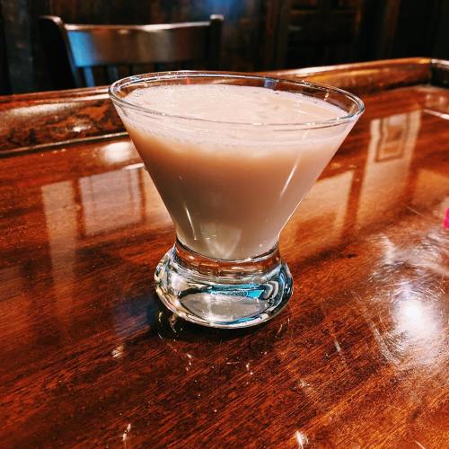 A creamy cocktail in a stylish glass sits on a wooden table, reflecting warm light.