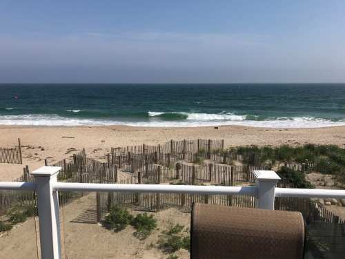 A serene beach view with gentle waves, sand, and wooden fencing under a clear blue sky.