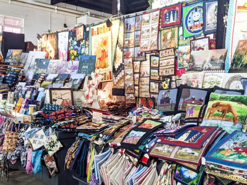 A vibrant display of handmade crafts and textiles, featuring colorful quilts, wall hangings, and various fabric items.