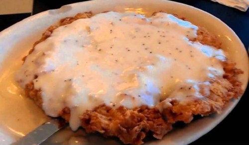 A plate of crispy fried chicken smothered in creamy white gravy.