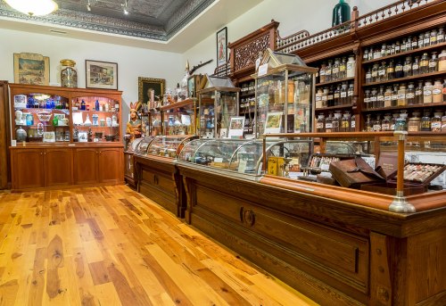 A vintage apothecary shop with wooden displays, glass jars, and shelves filled with various bottles and artifacts.