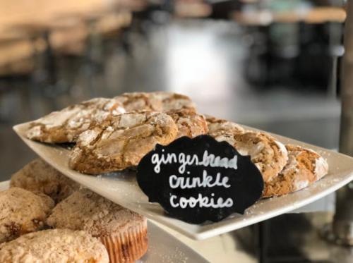 A plate of gingersnap crinkle cookies dusted with powdered sugar, displayed in a cozy café setting.