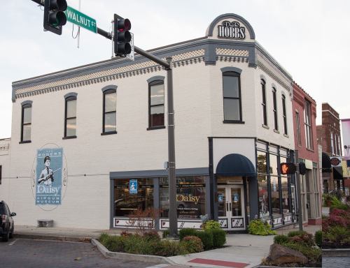 Historic building with a mural, featuring a sign for Hobbs' Daisy Airgun Museum, located at a street intersection.