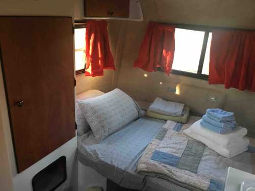 Cozy interior of a small camper with a bed, neatly arranged towels, and bright red curtains.