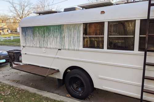 A white bus with colorful paint drips on the side, parked on a residential street.