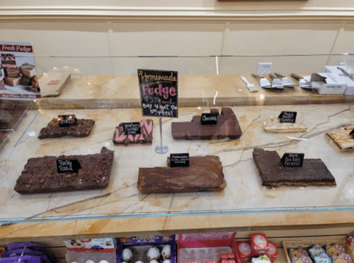 A display case filled with various types of fudge, labeled with names like "Rocky Road" and "Peanut Butter."