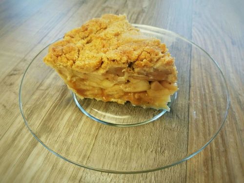 A slice of apple pie on a clear glass plate, resting on a wooden table.