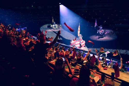 Audience waves flags while watching a performance featuring horses and riders under dramatic lighting.